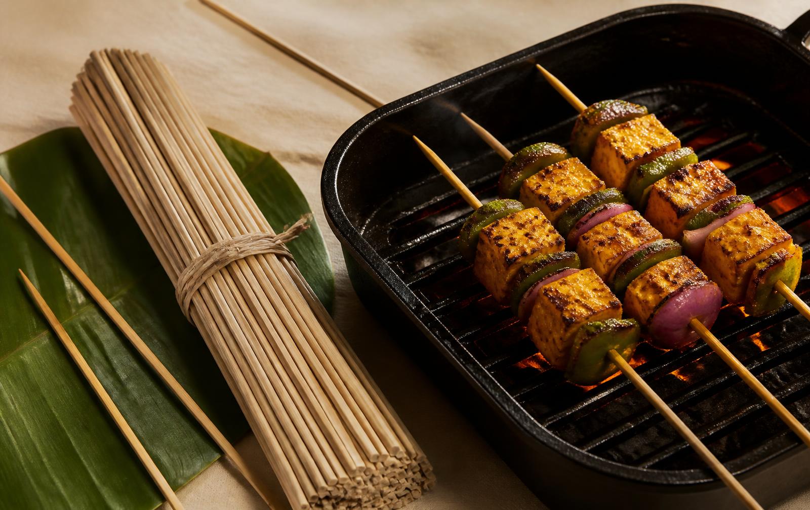 Natural bamboo barbeque sticks beside a grill with paneer tikka skewers over charcoal, made by GreenLife Bamboo